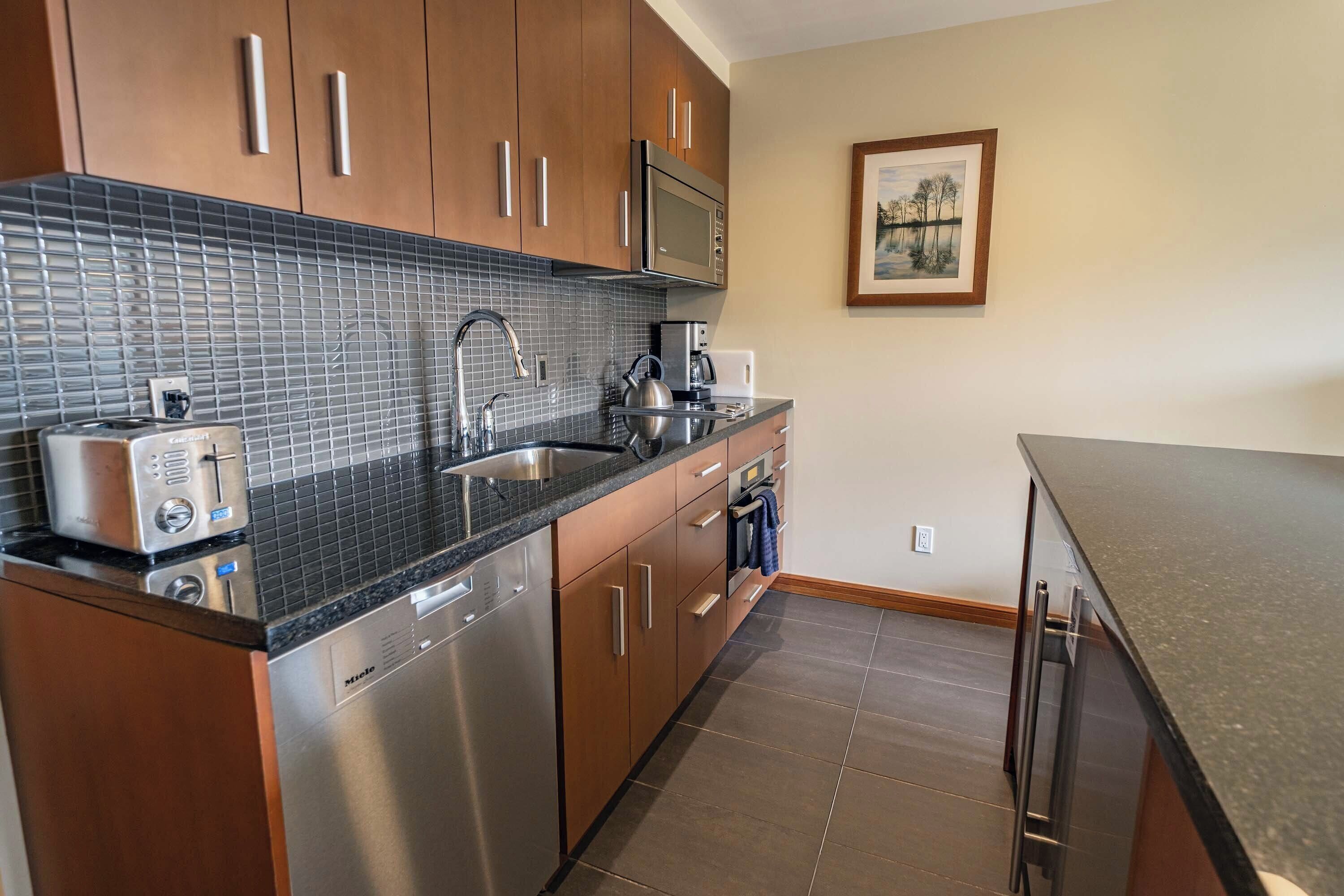 A modern kitchen with stainless steel appliances, a tiled backsplash, wooden cabinets, and a framed picture on the wall.