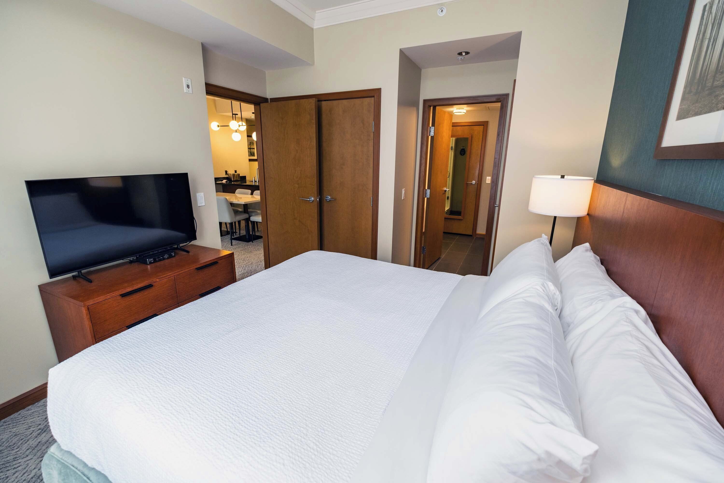 A hotel room with a bed, a TV on a wooden dresser, a lamp, and a mirror.