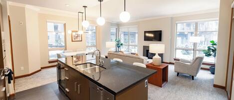 A modern kitchen with a central island, a dining area with a sofa and chairs, and large windows offering views of the city.