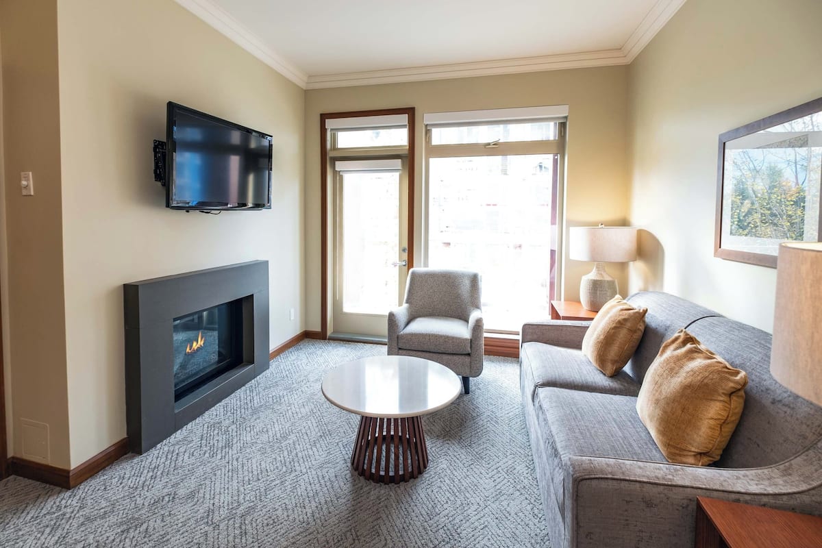 Een woonkamer met een open haard, een flatscreen televisie, een grijze bank en een ronde salontafel.