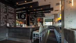 Eine Bar mit einer langen Theke, mehreren Barhocker und einer Wandtafel mit Getränke- und Bierauswahl.