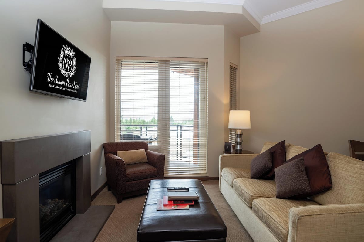 Een woonkamer met een open haard, een bank, een stoel en een flatscreen-tv aan de muur, waarop de naam van het hotel staat.