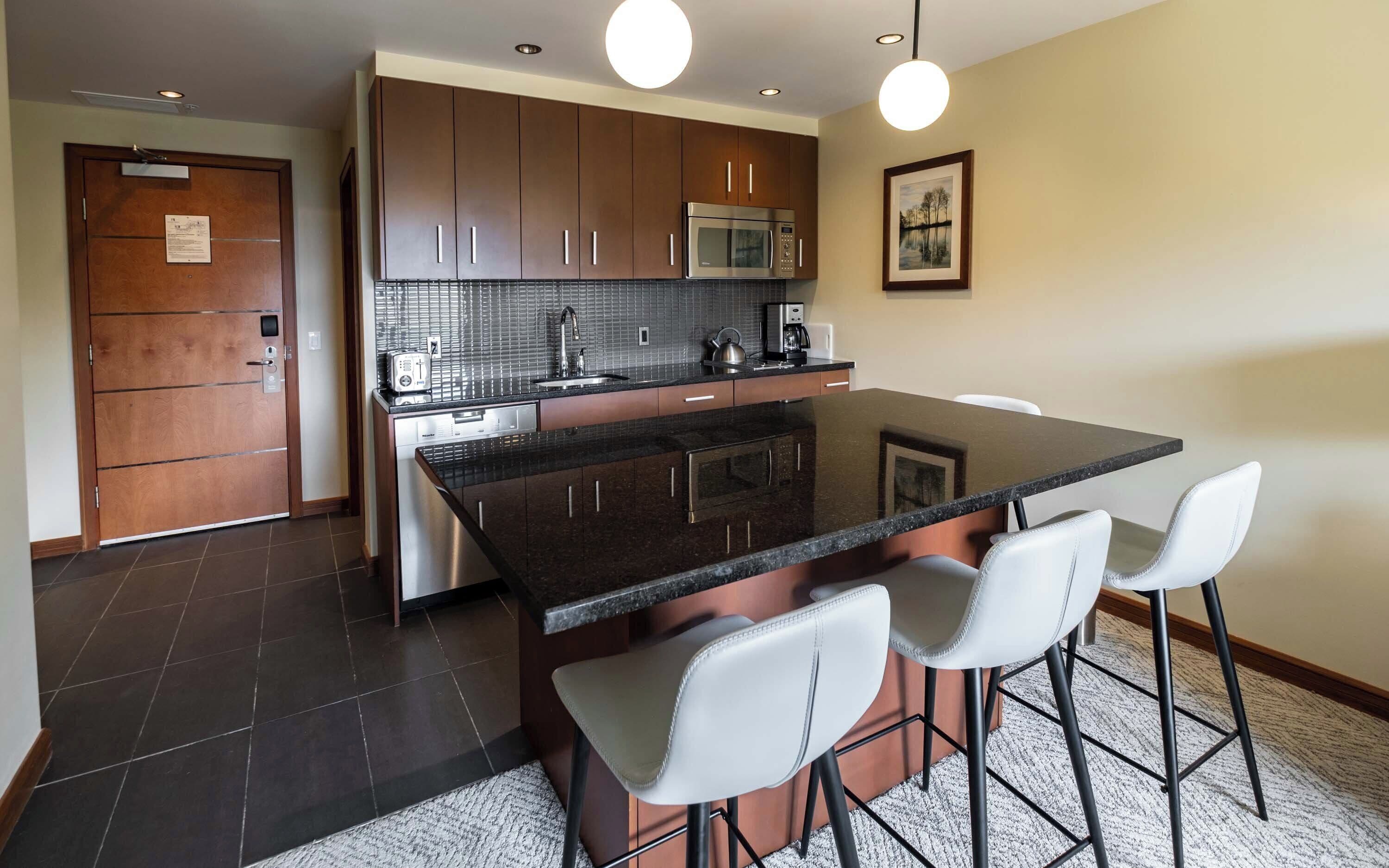 A modern kitchen with dark cabinetry, a central island with bar stools, a microwave, and a coffee maker.