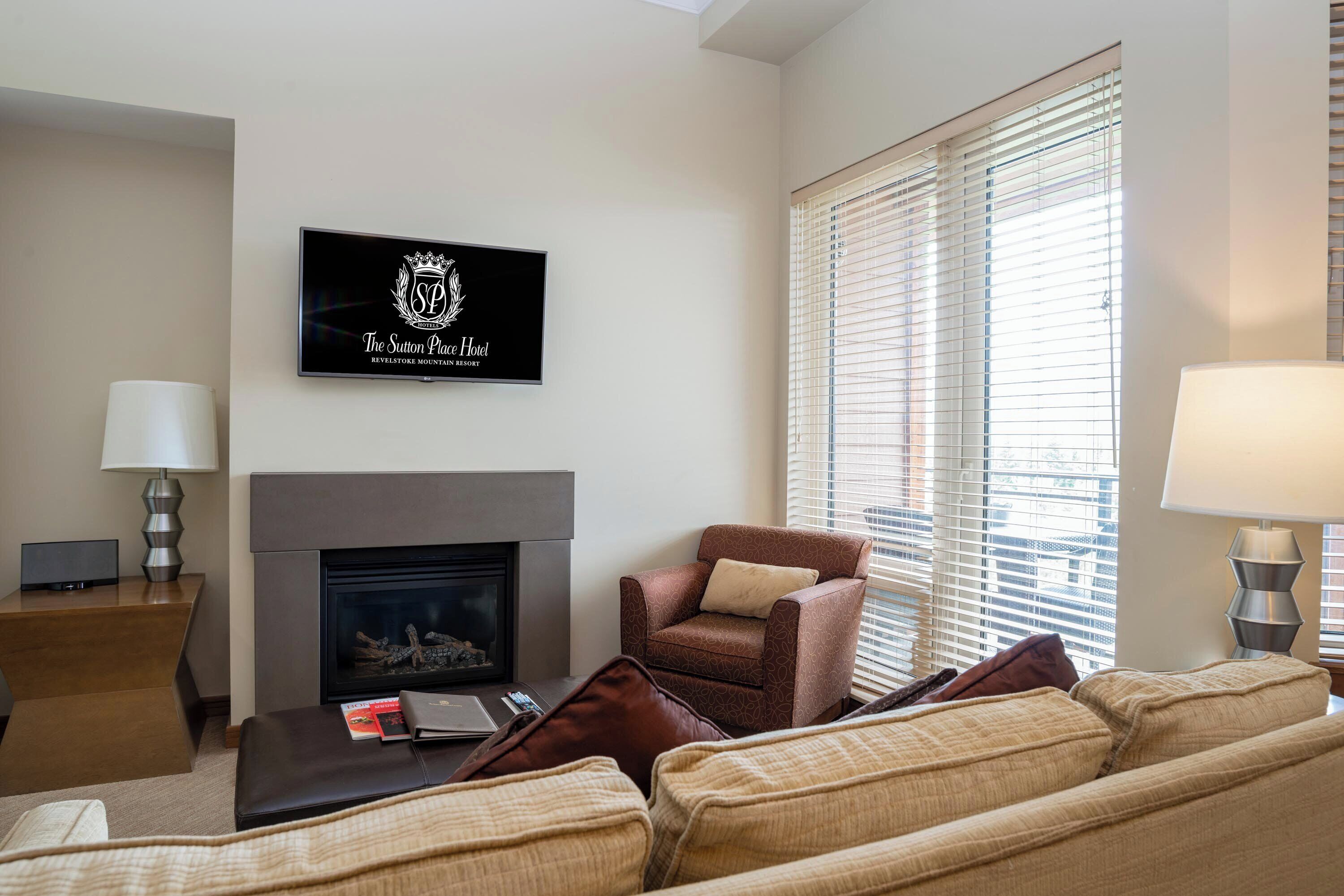 A living room with a fireplace, a sofa, a chair, and a television displaying "The Sutton Place Hotel" logo.