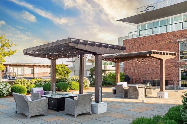 Une terrasse extérieure aménagée avec des meubles en osier, un foyer et une structure en forme de pergola.