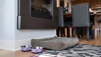 A pet bed, two pet bowls, and a window with a view of a dining area.