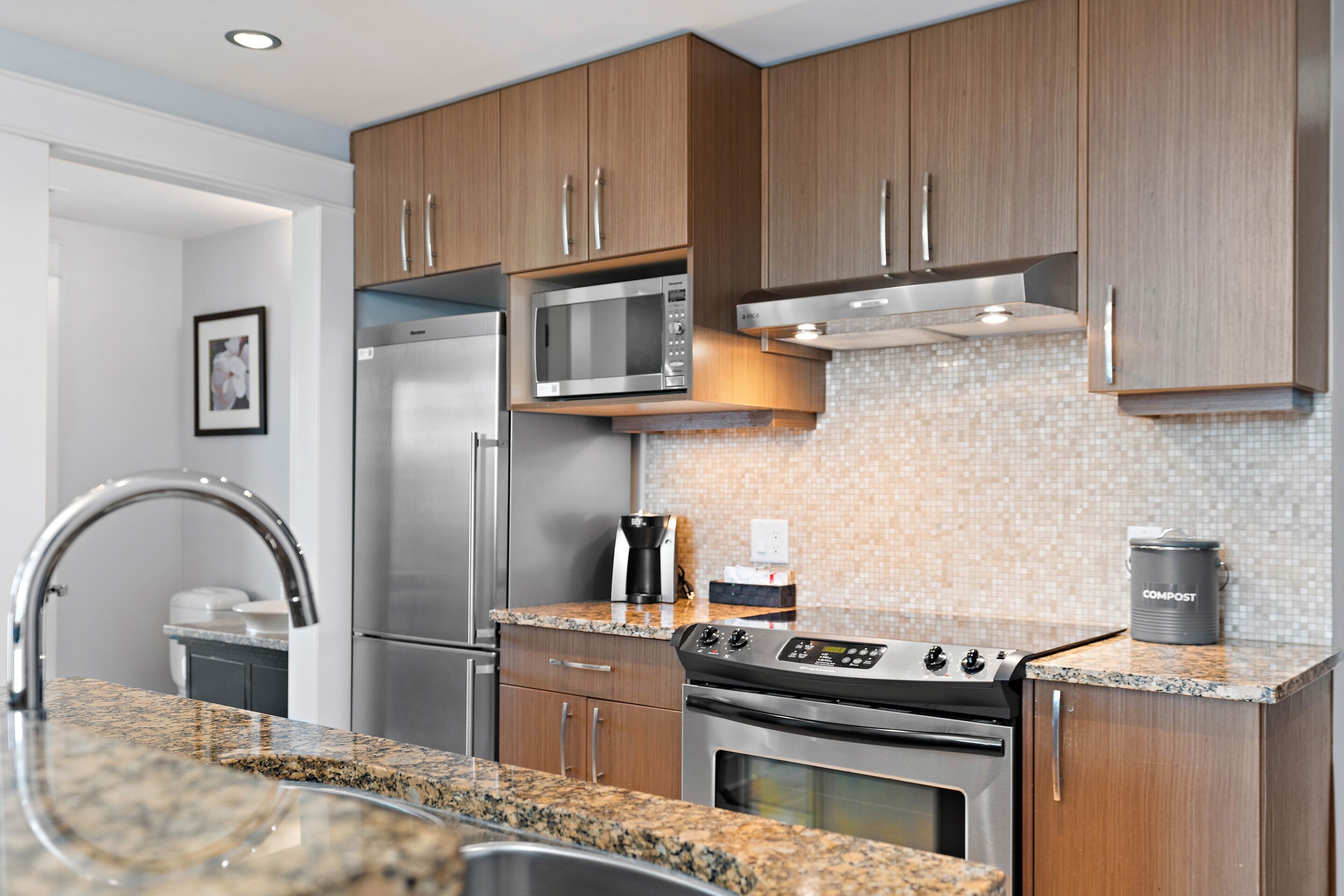 Una cocina moderna con electrodomésticos de acero inoxidable, armarios de madera, encimeras de granito y salpicadero de azulejos.