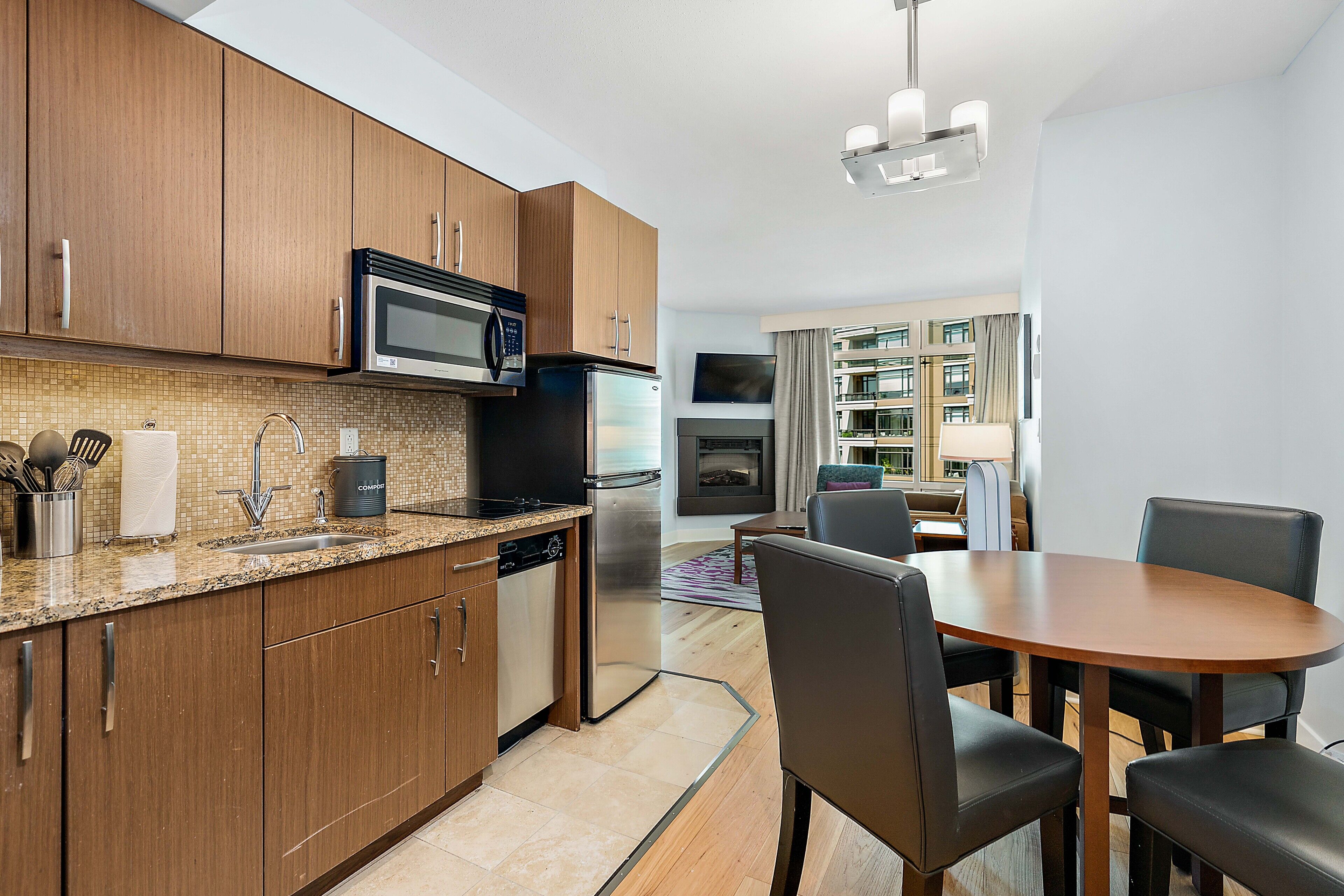A modern kitchen with wooden cabinets, stainless steel appliances, and a dining area with a round table and chairs.