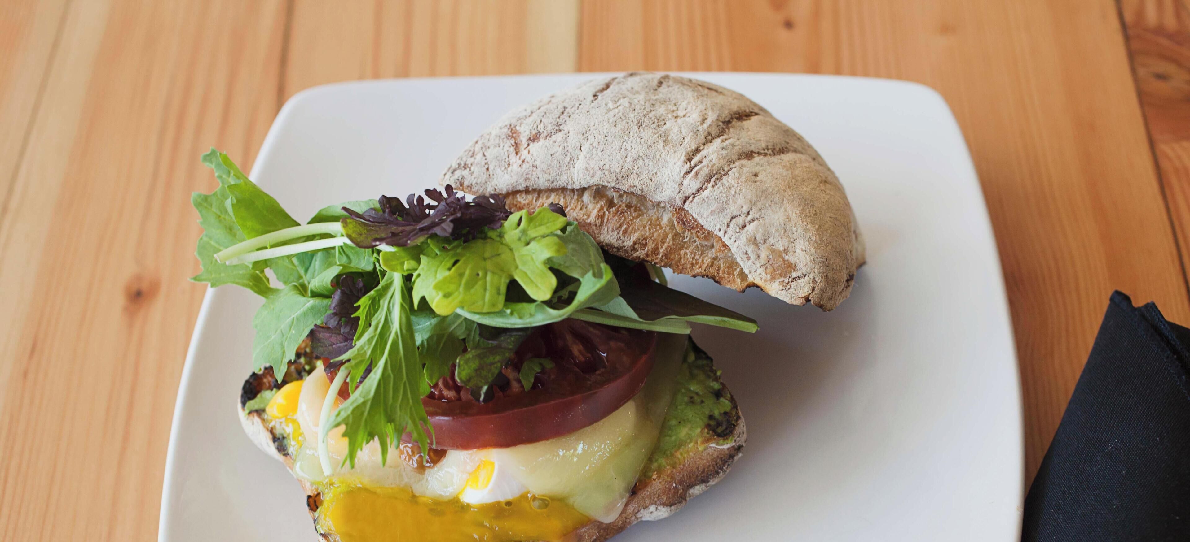 A sandwich on a white plate with a piece of bread on the side.