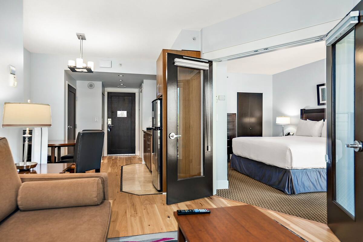 A hotel room with a bed, bedside table, lamp, and a view of the hallway.