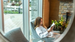 A spa area with a stone fireplace, a comfortable chair, and a window with a view of the spa entrance.