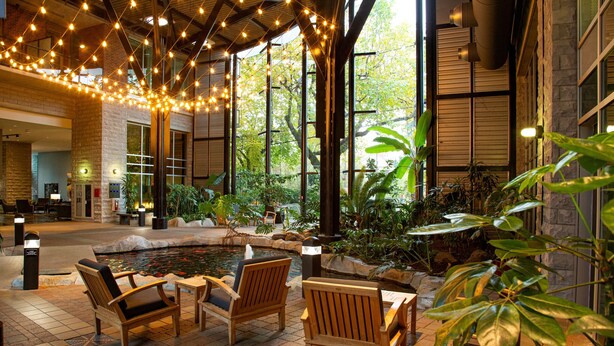 A spacious indoor area with a koi pond, wooden chairs, and string lights.