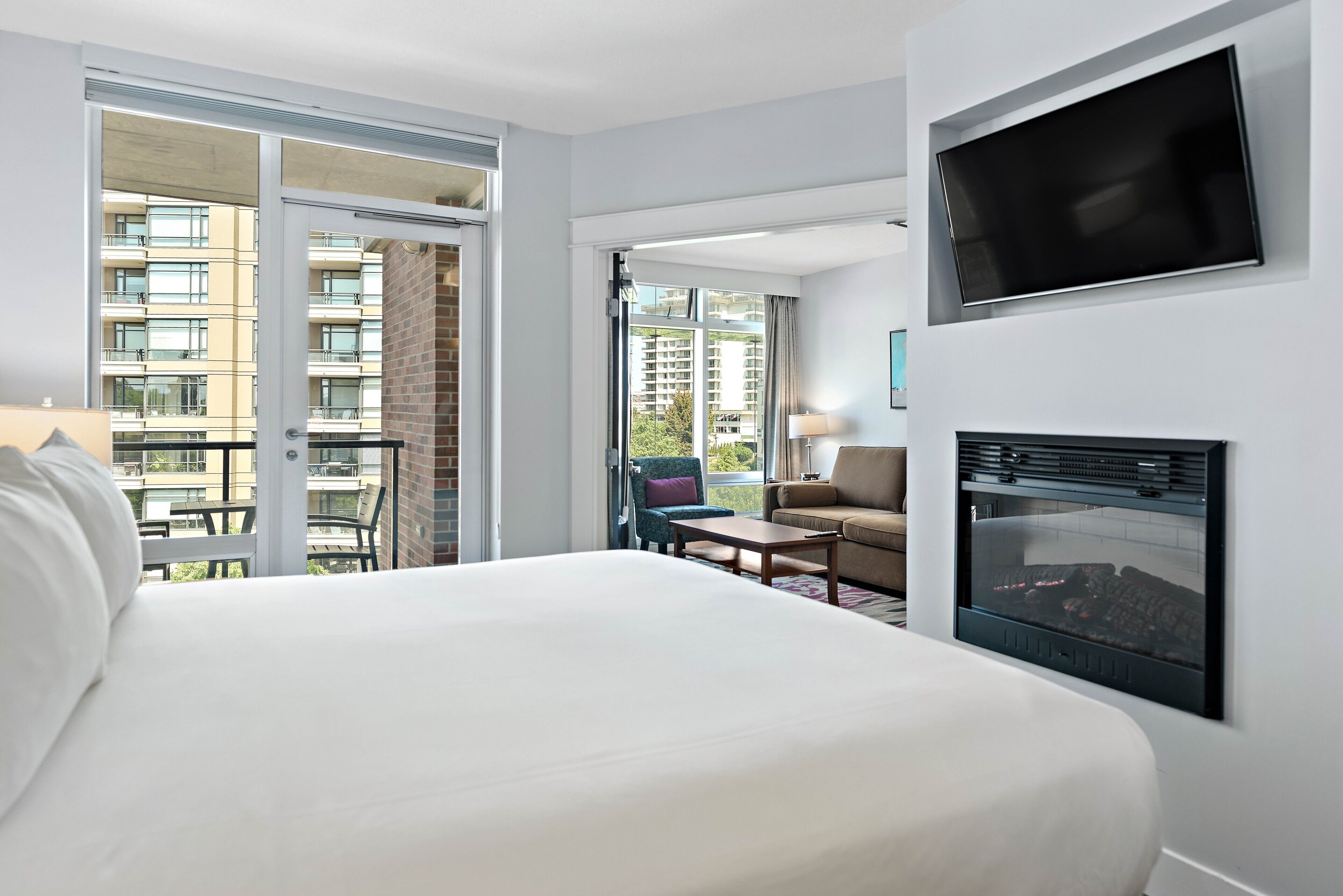 Une chambre d’hôtel dotée d’un grand lit, d’un téléviseur fixé au mur, d’une cheminée et d’un balcon offrant une vue sur les autres bâtiments.