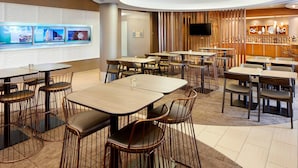 A hotel dining area with multiple tables and chairs, a television mounted on the wall, and a bar area with stools. - SpringHill Suites by Marriott Houston NASA/Webster (Webster)