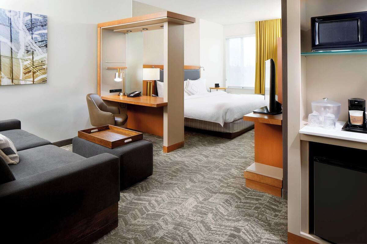 A hotel room with a bed, a desk with a computer, a chair, a sofa, and a television.