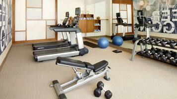 A gym with treadmills, a bench press, dumbbells, exercise balls, and a mirrored wall.