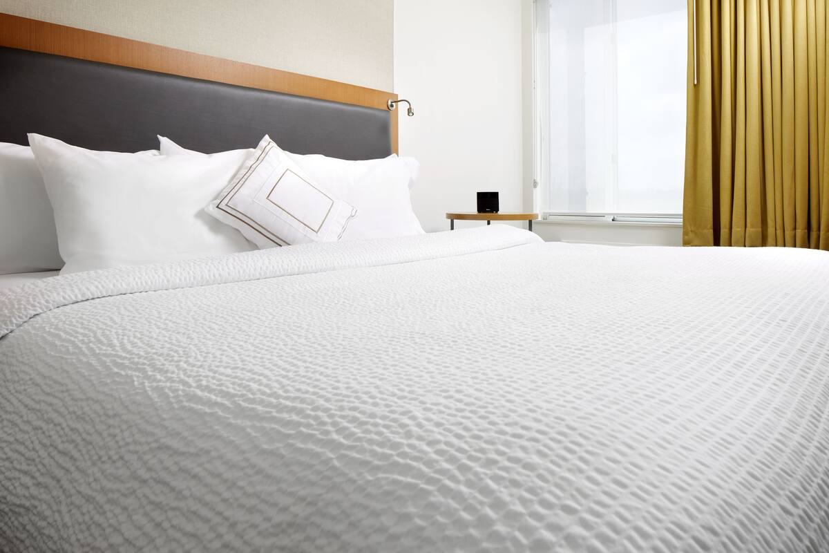 A neatly made bed with white bedding, a wooden headboard, and a small bedside table with a black object.