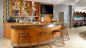 A bar area with a wooden counter, bar stools, and a television mounted above the bar. - SpringHill Suites by Marriott Houston NASA/Webster (Webster)