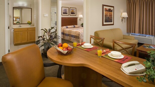 A hotel room with a wooden dining table, chairs, a telephone, and a bed with a headboard. - Candlewood Suites Jacksonville by IHG (Jacksonville)