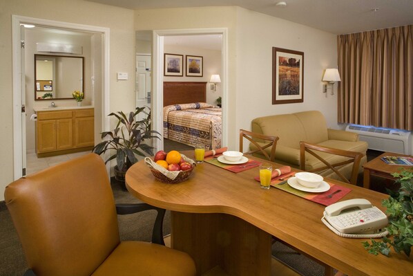 A hotel room with a wooden dining table, chairs, a telephone, and a bed with a headboard. - Candlewood Suites Jacksonville by IHG (Jacksonville)