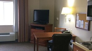 A hotel room with a desk, chair, television, lamp, and kitchenette. - Candlewood Suites Jacksonville by IHG (Jacksonville)