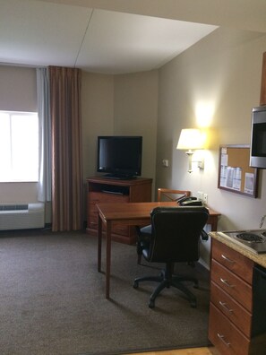 A hotel room with a desk, chair, television, lamp, and kitchenette. - Candlewood Suites Jacksonville by IHG (Jacksonville)