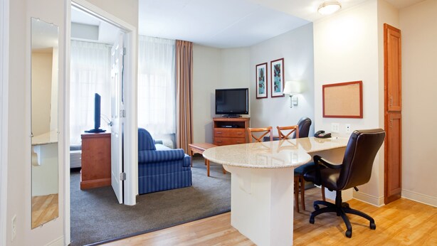 A hotel room with a living area, a dining table with chairs, a TV, and a small kitchenette. - Candlewood Suites Jacksonville by IHG (Jacksonville)
