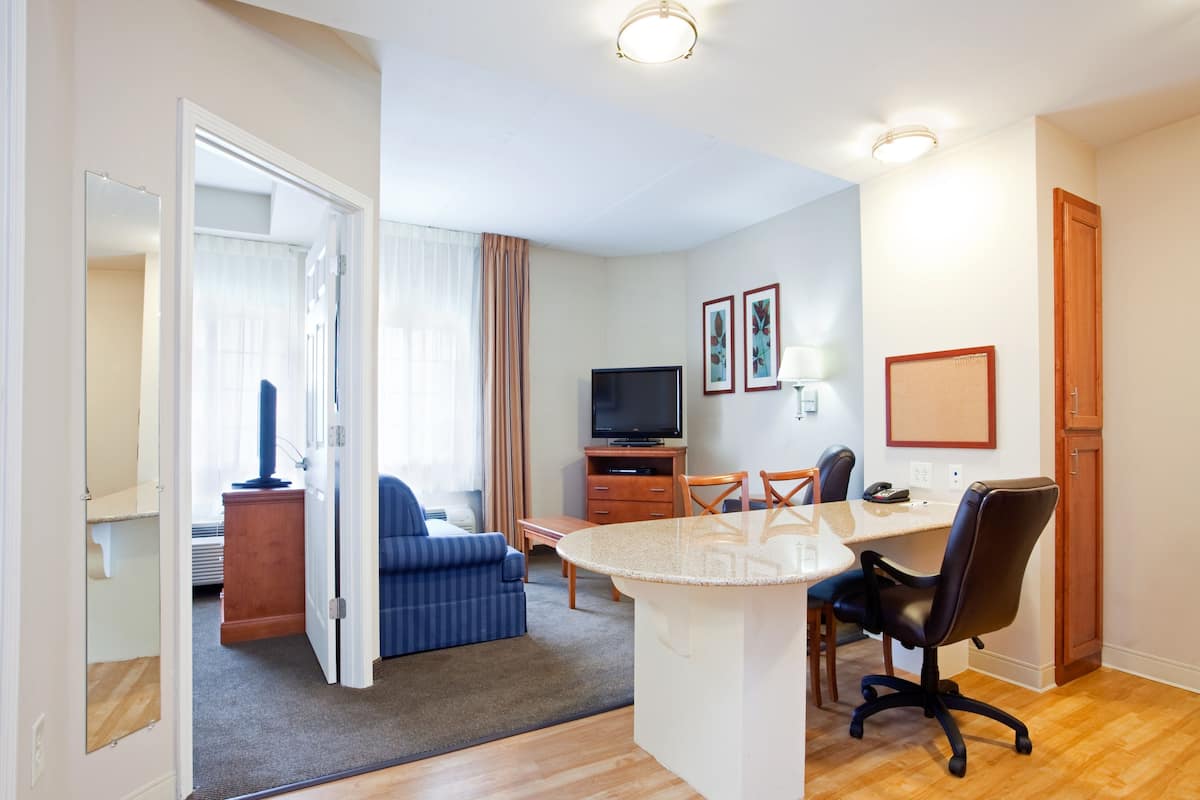 A hotel room with a living area, a dining table with chairs, a TV, and a small kitchenette.