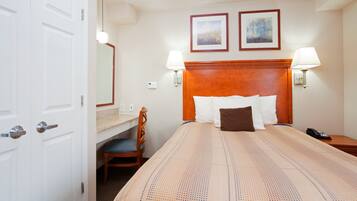 A hotel room with a bed, bedside lamps, a desk with a chair, a telephone, and two framed pictures on the wall.
