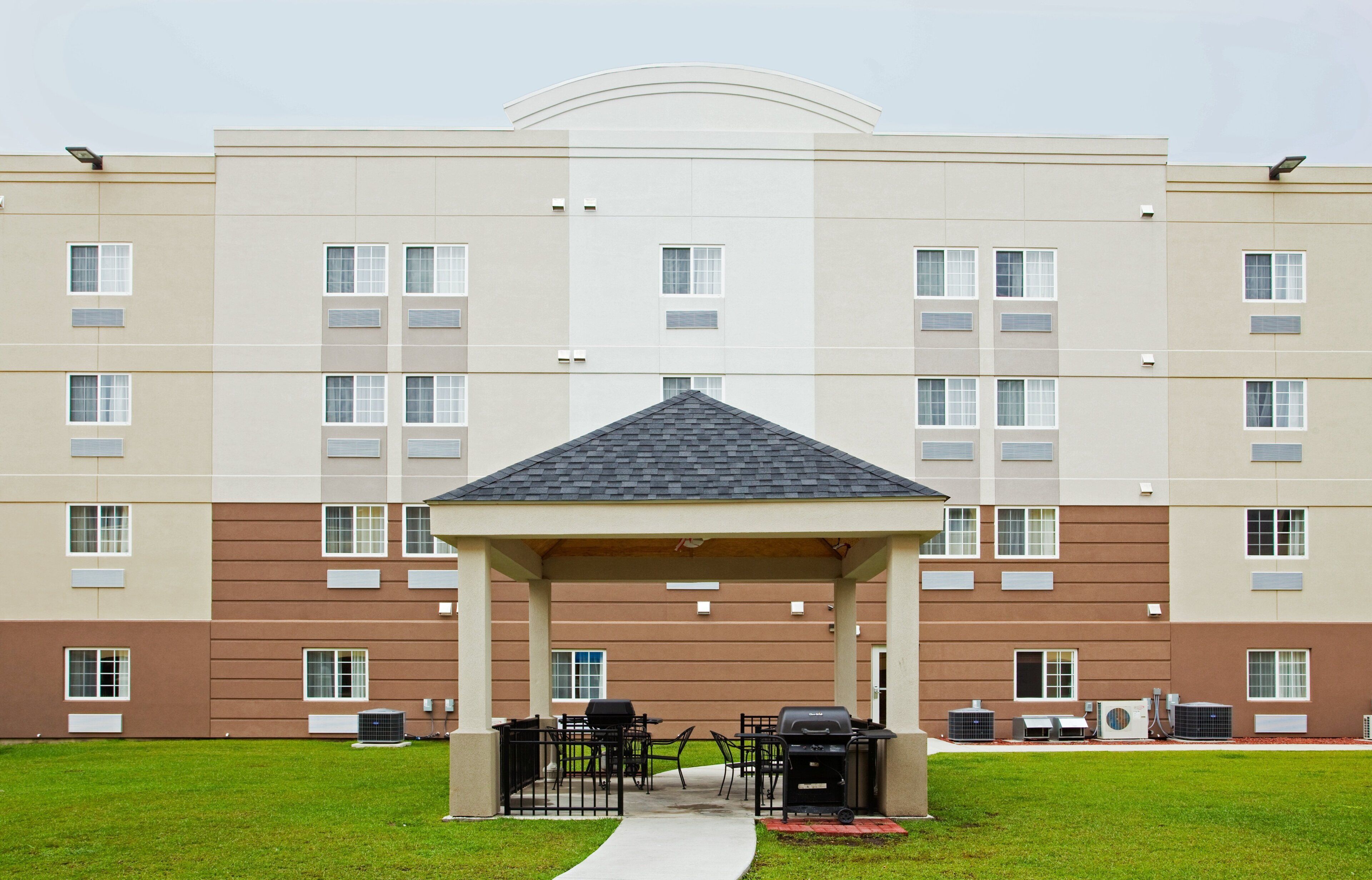 A multi-story building with a covered outdoor seating area, air conditioning units, and a clear sky.