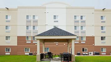 A multi-story building with a covered outdoor seating area, air conditioning units, and a clear sky.