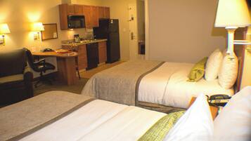 A hotel room with two beds, a desk, a chair, a microwave, a refrigerator, and a lamp.