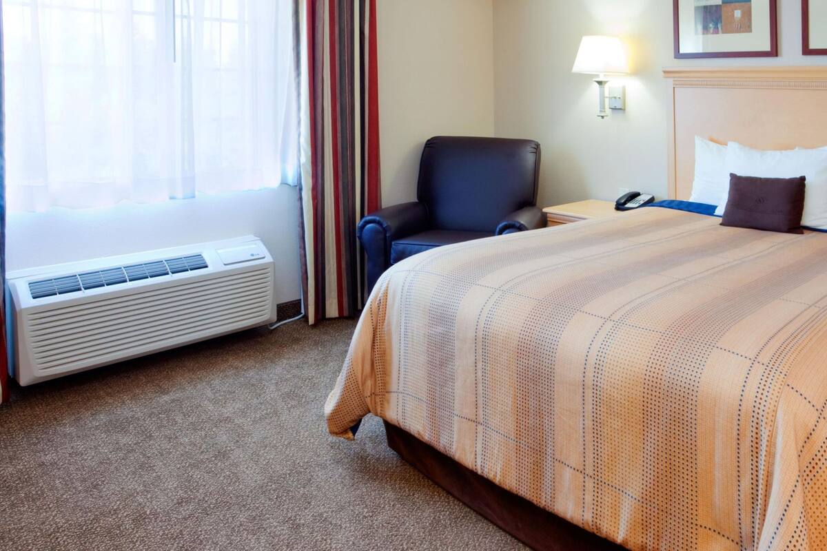 A hotel room with a large bed, a chair, a desk, and a window with curtains.