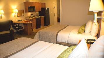 A hotel room with two beds, a desk, a microwave, and a refrigerator.