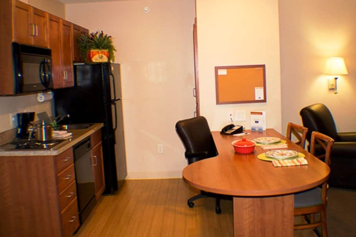 A compact kitchen with a microwave, stove, and cabinets. There's a dining table with chairs and a small refrigerator.