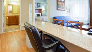 A hotel room with a kitchen area, a dining table with chairs, a bed with a headboard, a blue sofa, and a window with curtains. - Candlewood Suites Jacksonville by IHG (Jacksonville)