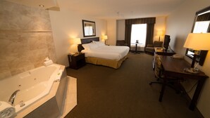 Quarto de hotel com uma cama grande, uma área de estar separada com escrivaninha e cadeira, banheira e uma mesinha de cabeceira com abajur.