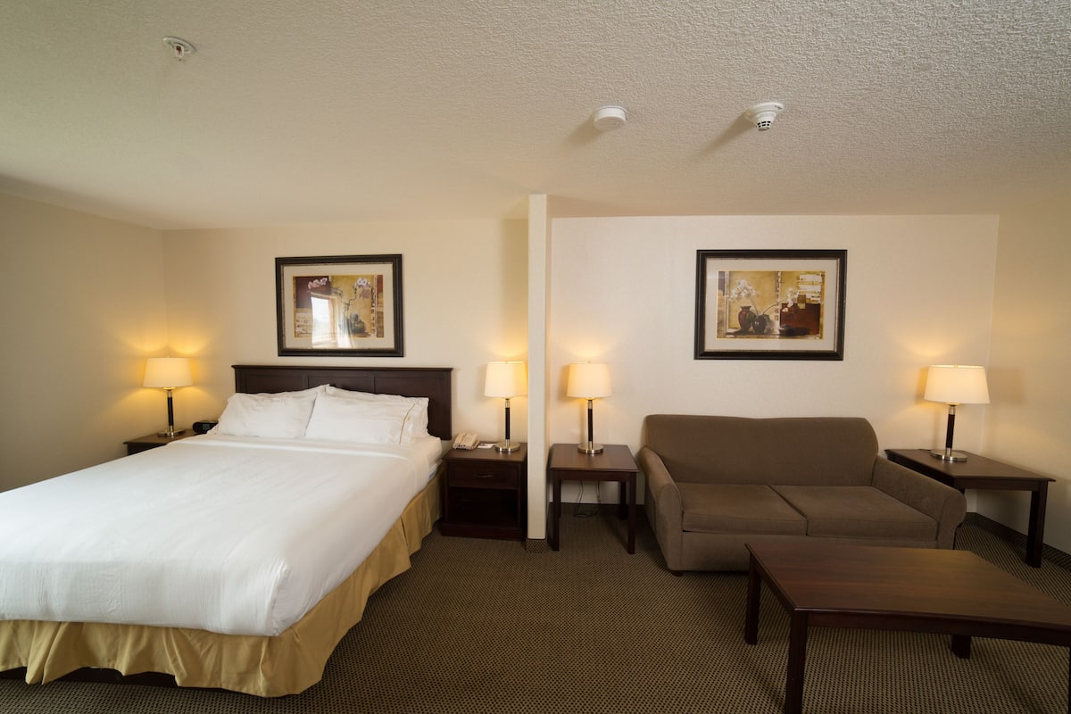 A hotel room with a bed, a sofa, a small table, and two nightstands with lamps.