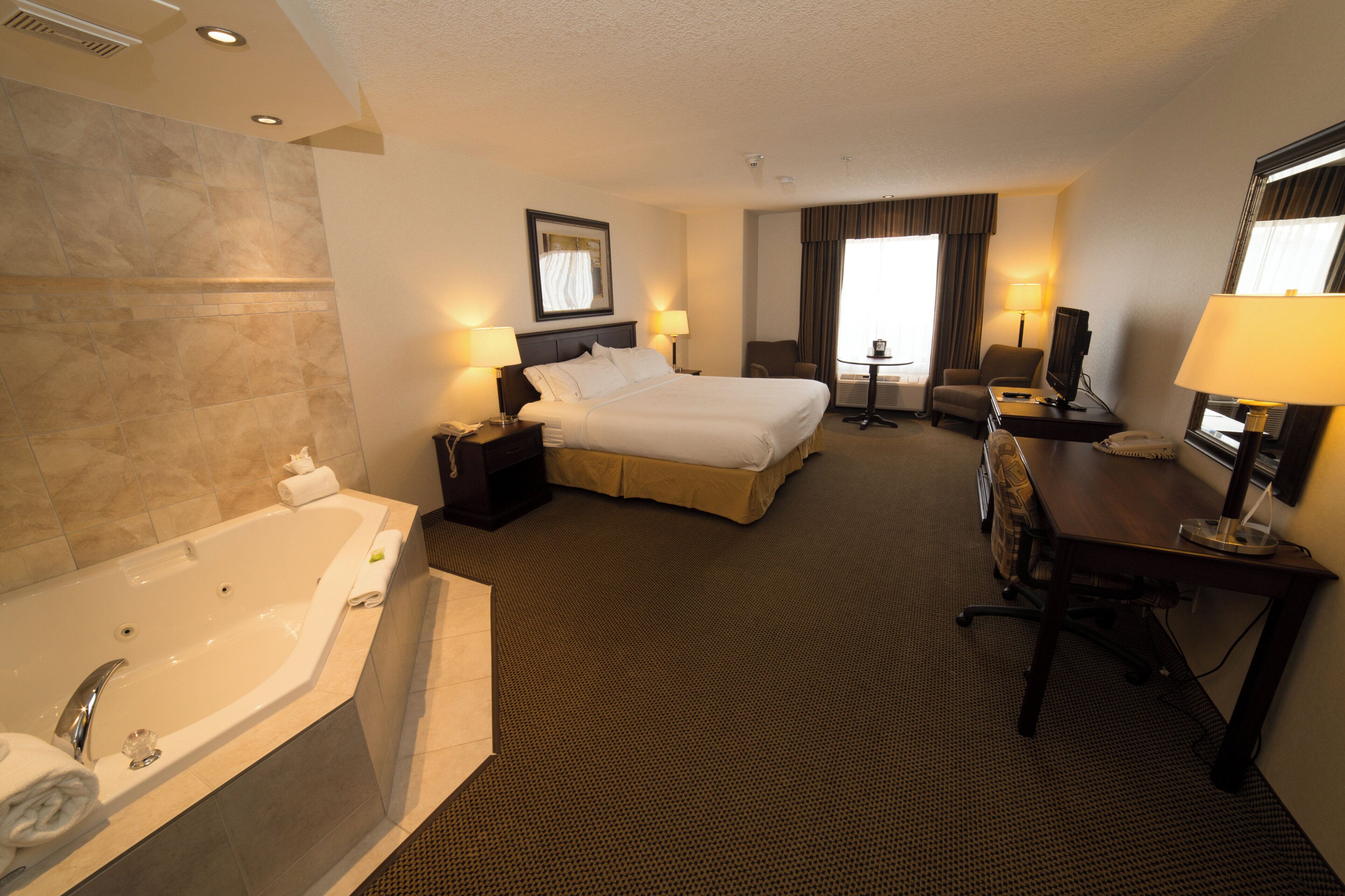 A hotel room with a large bed, a separate sitting area with a desk and chair, a television, and a bathroom with a bathtub.
