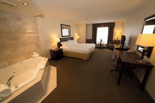 A hotel room with a large bed, a separate sitting area with a desk and chair, a television, and a bathroom with a bathtub.