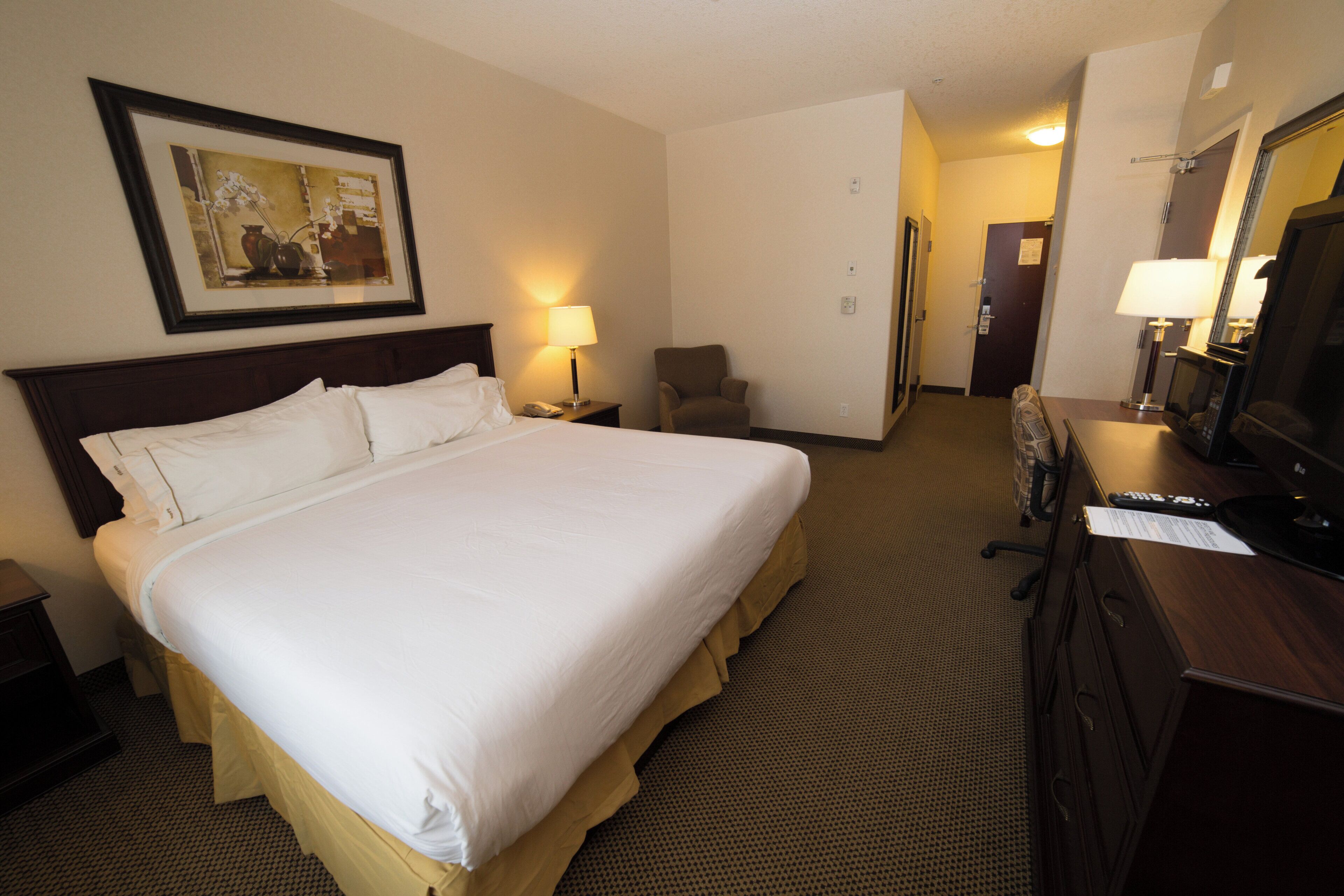 A hotel room with a large bed, a desk with a computer, a chair, a desk lamp, and a television.