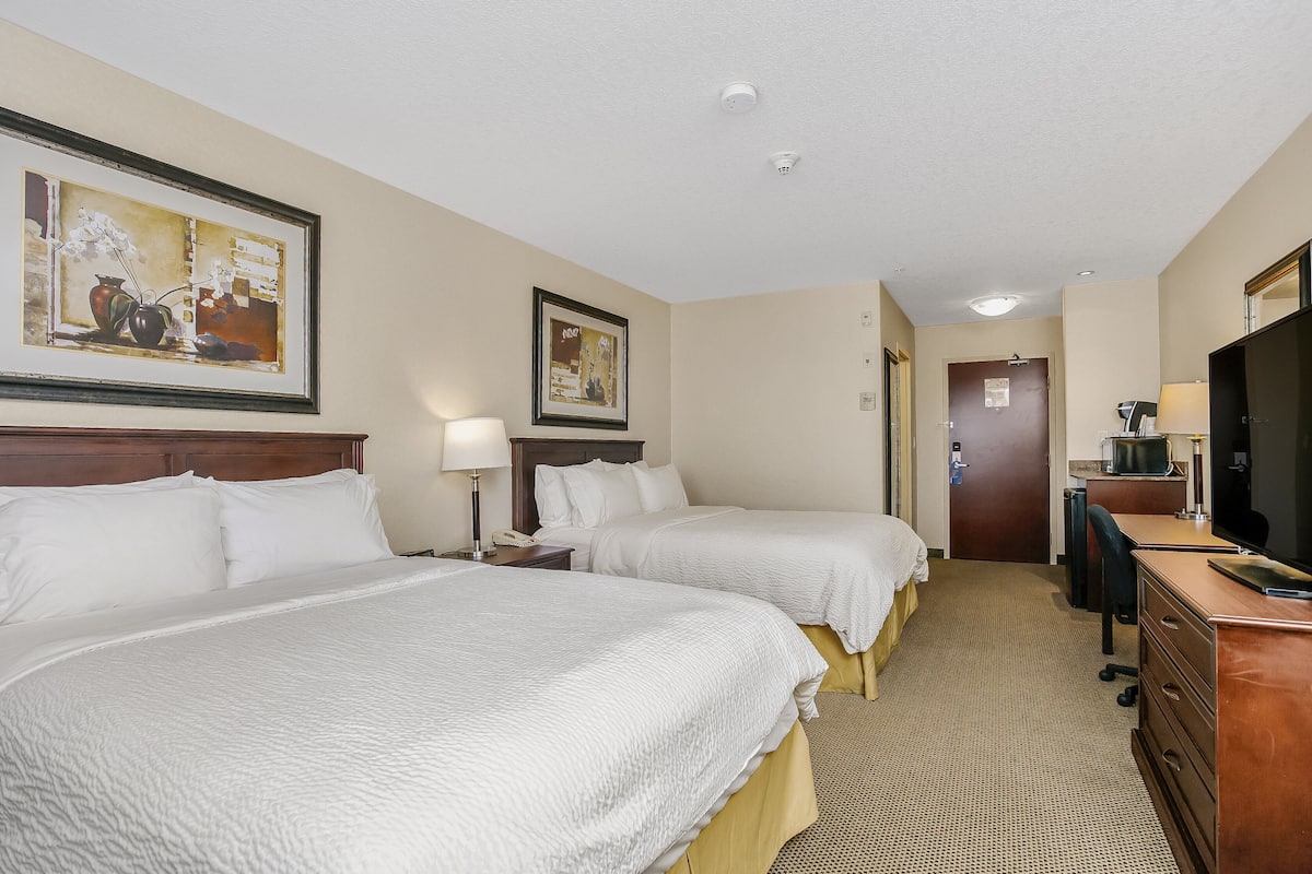 A hotel room with two beds, a desk, a TV, and a door leading to the bathroom.