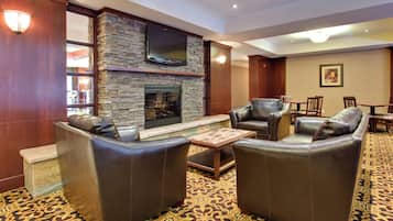A hotel lobby with leather sofas, a stone fireplace, a flat-screen TV, and a patterned carpet.