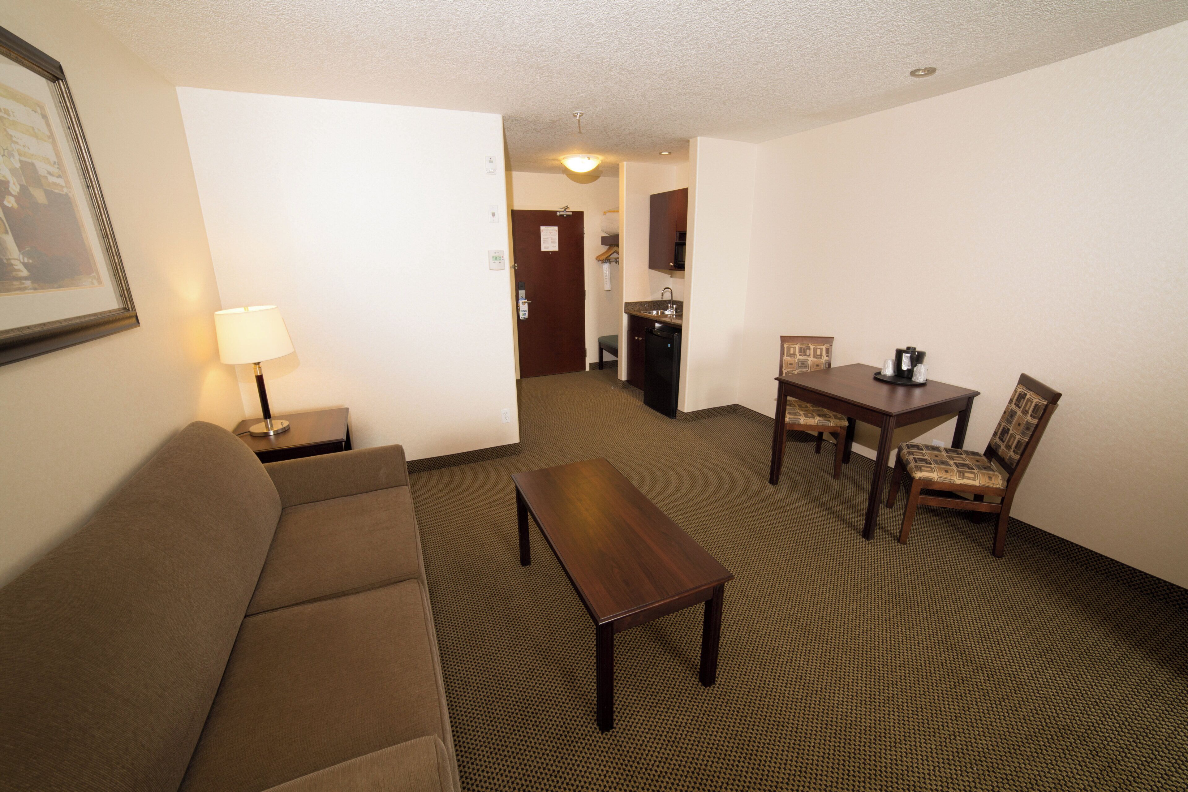 Habitación de hotel con sofá, una mesita, zona de comedor con mesa y sillas, y kitchenette.