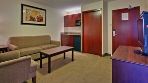 Uma sala de estar compacta com um sofá, uma mesinha e um espaço de cozinha americana com armários de madeira e micro-ondas.