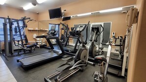 Uma academia com esteiras, aparelhos de musculação e halteres.
