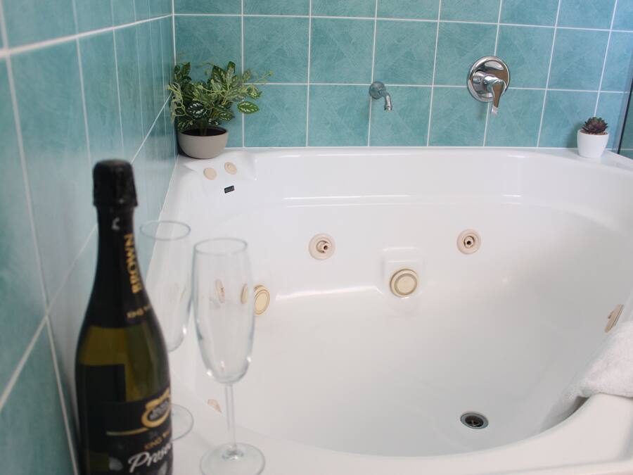 Eine Badewanne mit einer Weinflasche, einem Glas, einem Topfpflanzen und einem kleinen weißen Behälter am Rand.