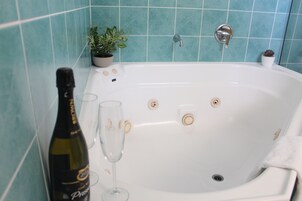 Une baignoire avec une bouteille de vin et un verre, une plante en pot et un petit récipient blanc posé sur le bord.