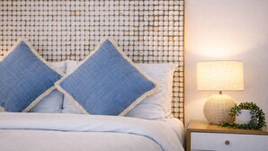 A bed with a headboard featuring a geometric pattern, a bedside lamp, and a small potted plant. - At The Sound (Noosaville)
