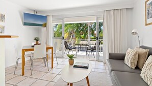 A modern living room with a dining area, a balcony with a view of greenery, and a sofa with decorative pillows. - At The Sound (Noosaville)